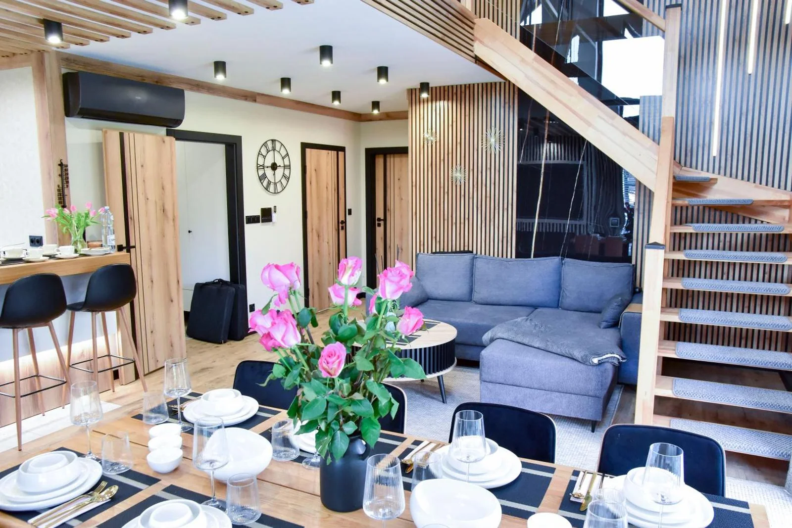Salon i jadalnia domu 4B — szara sofa, drewniane schody i nakryty stół
