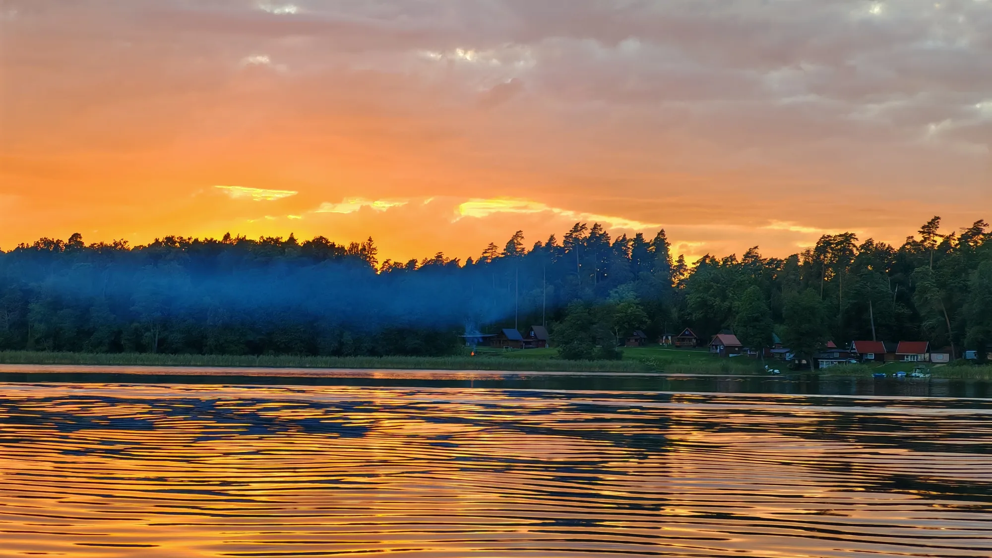 Zachód słońca nad mazurskim jeziorem — pomarańczowe niebo nad linią lasu odbite w wodzie
